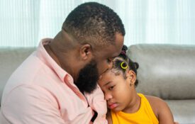 A fathering sitting on a couch and comforting his sad daughter.