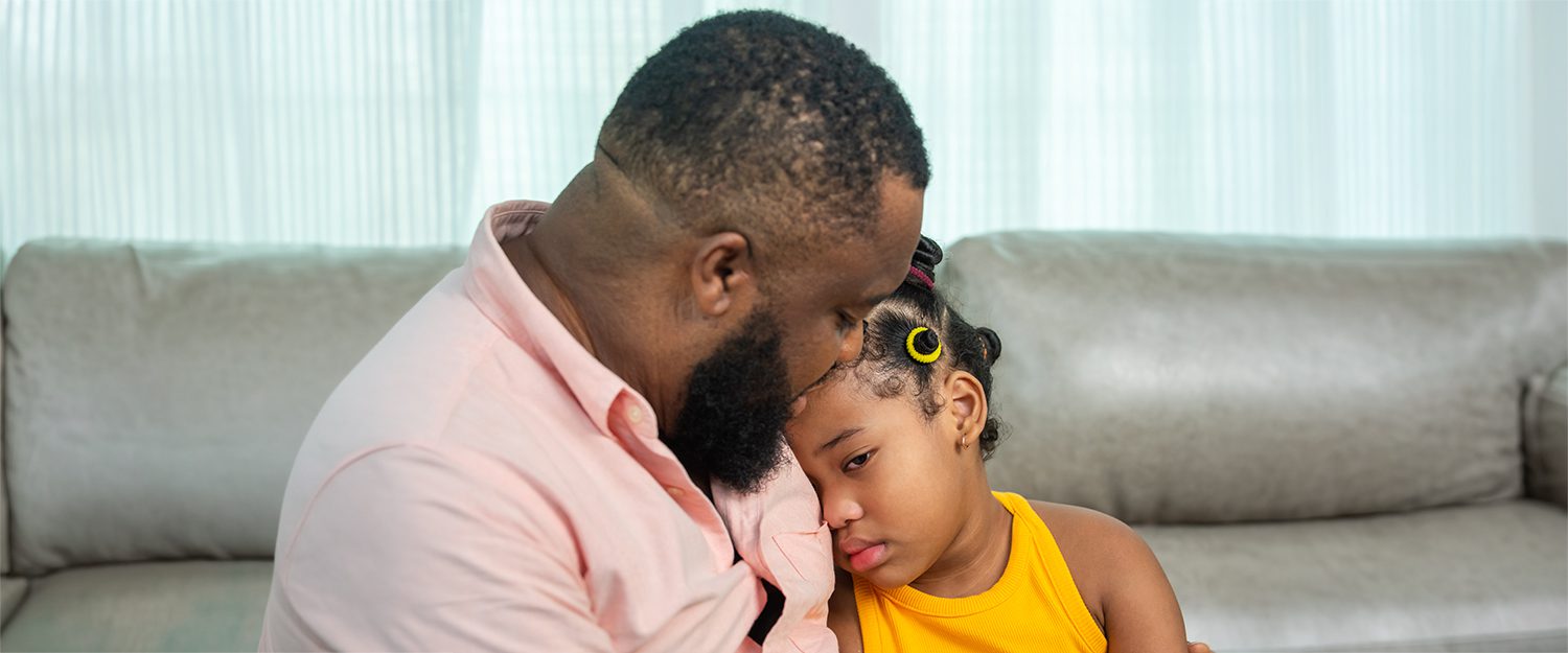 A fathering sitting on a couch and comforting his sad daughter.