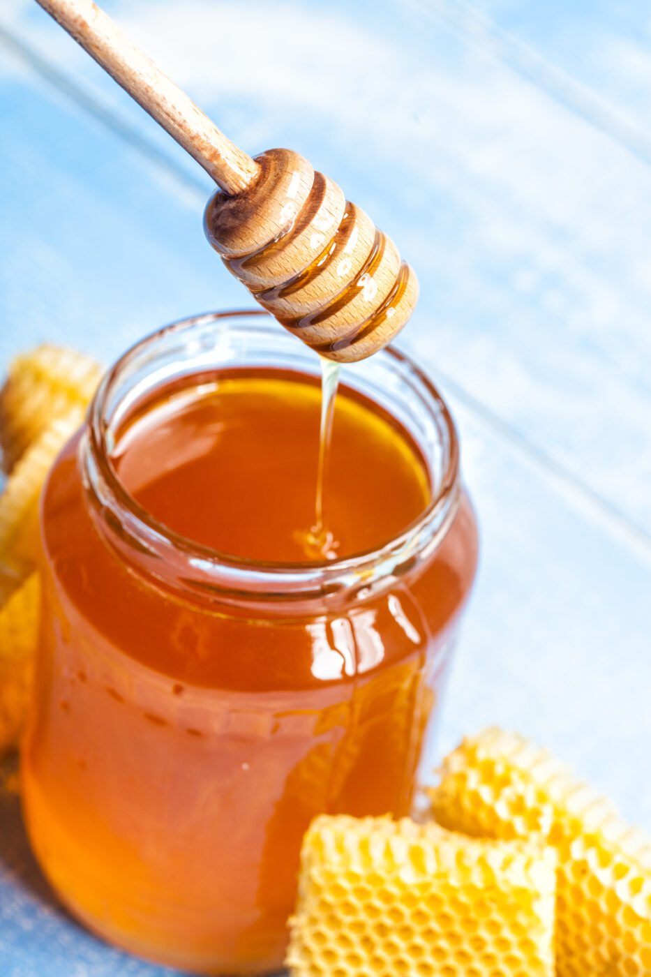 An open jar of honey with a wooden dipper and honeycomb.